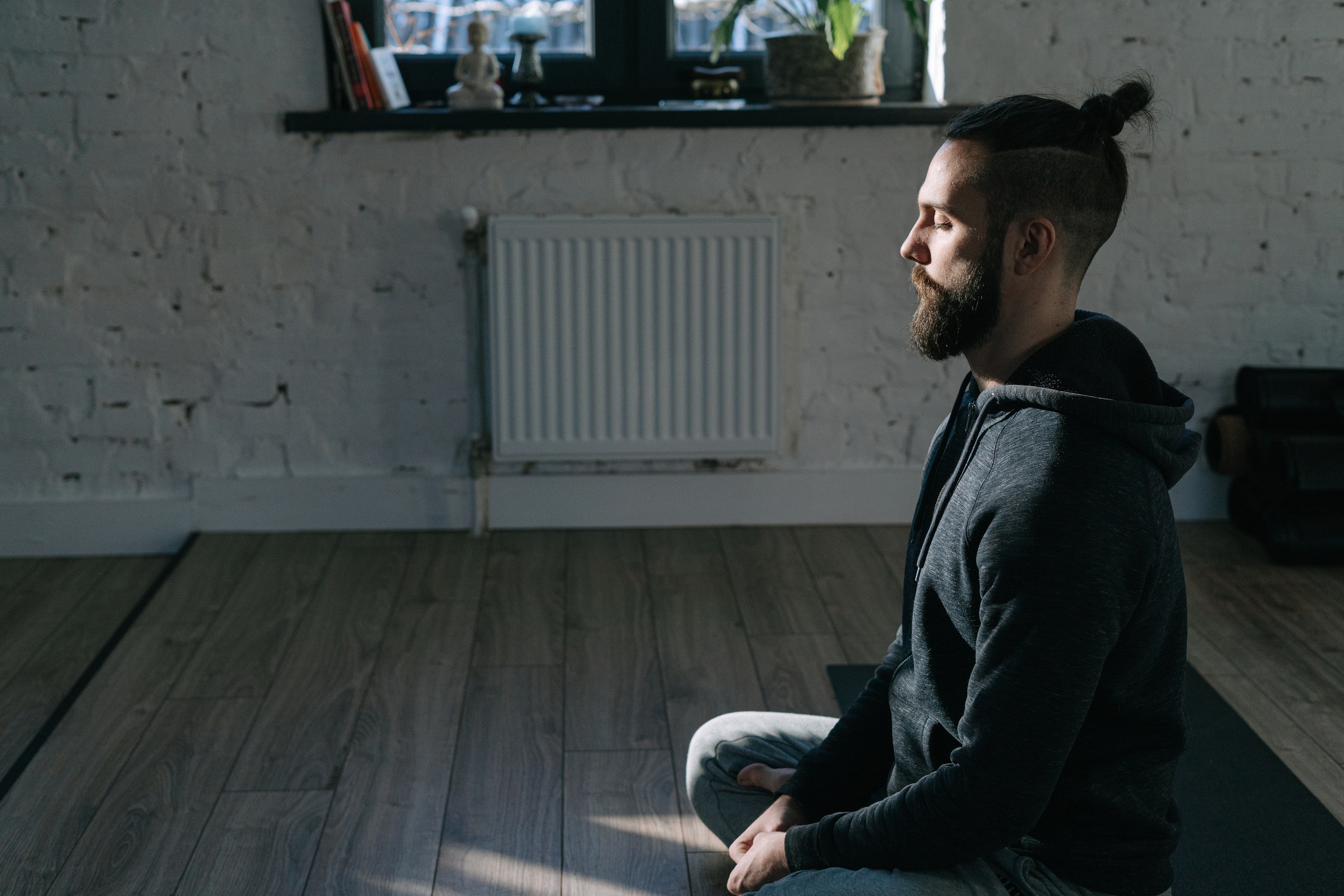 A man in a hoodie sweater meditating over a yoga mat