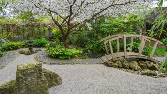 A Japanese garden with water features, cherry blossom tree, and bridge