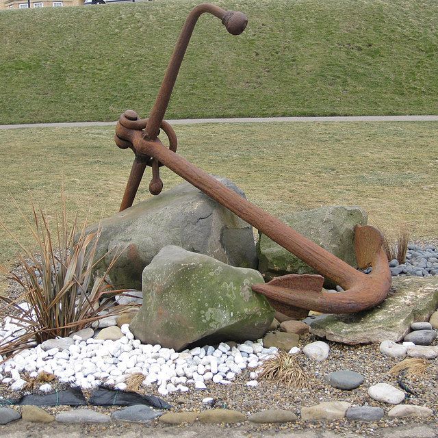 Rusty ship anchor on a flower or pebble bed